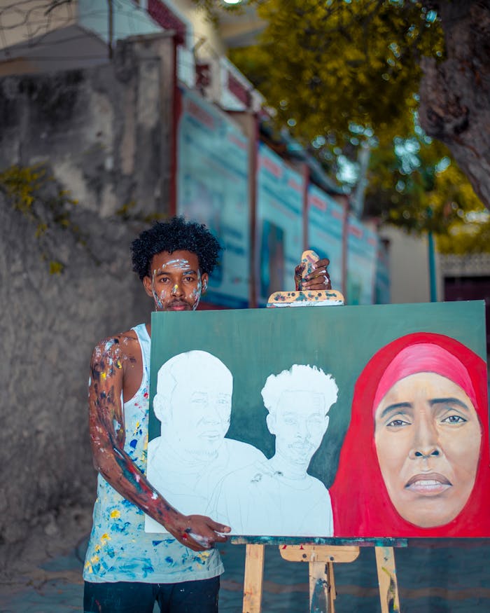 Young artist shows colorful unfinished portrait painting on a street in Somalia.